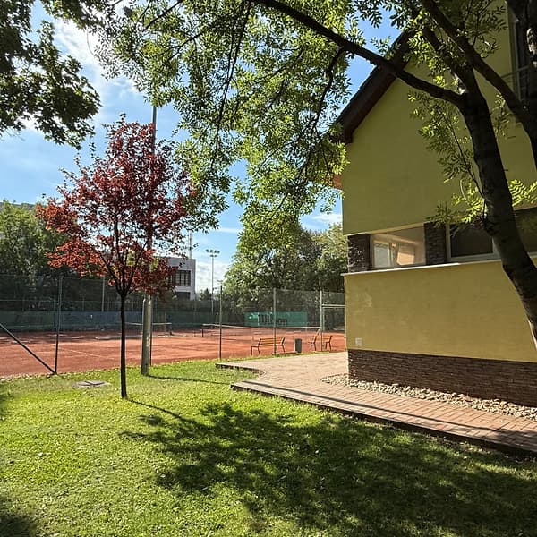 Trávnik s červeným stromom pri budove klubu TennisOne