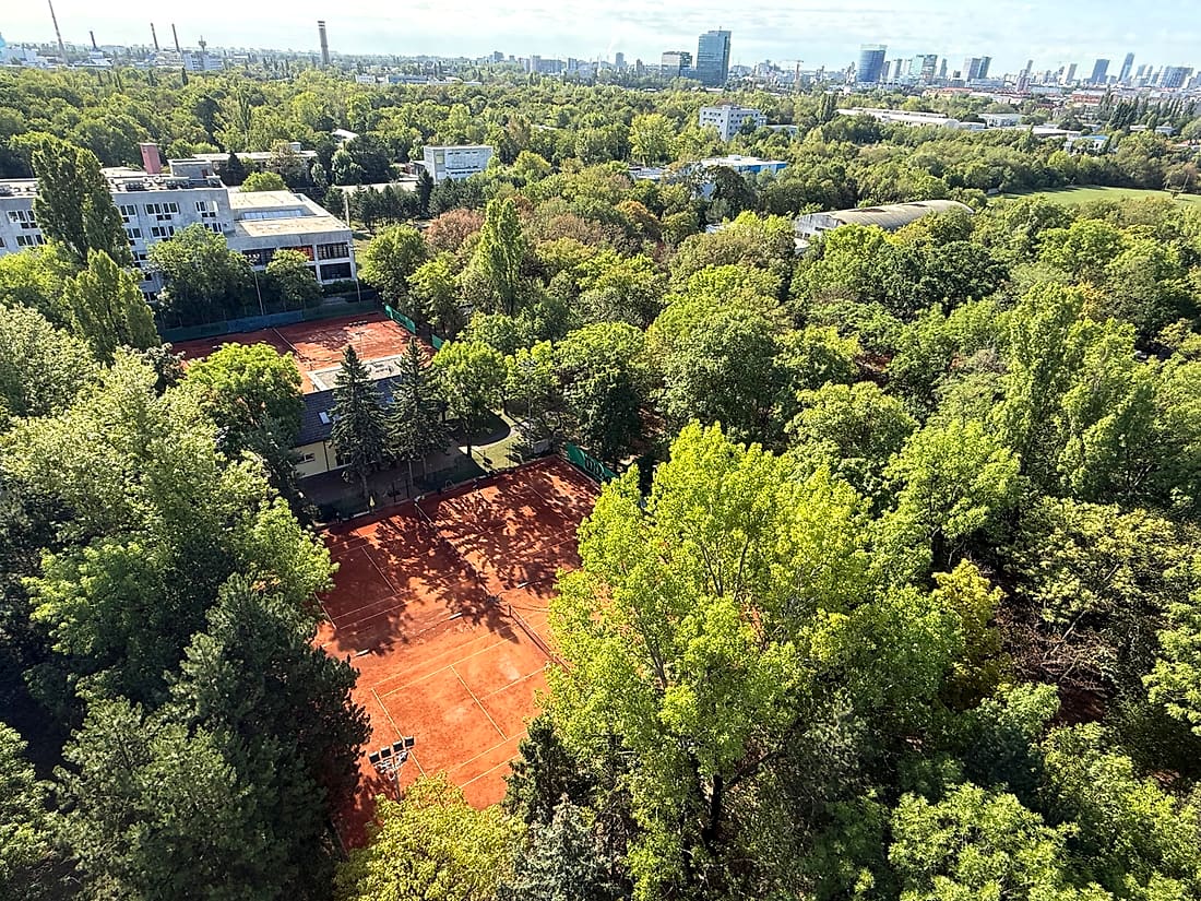 Pohľad zhora na antukové dvorce klubu TennisOne obklopené stromami